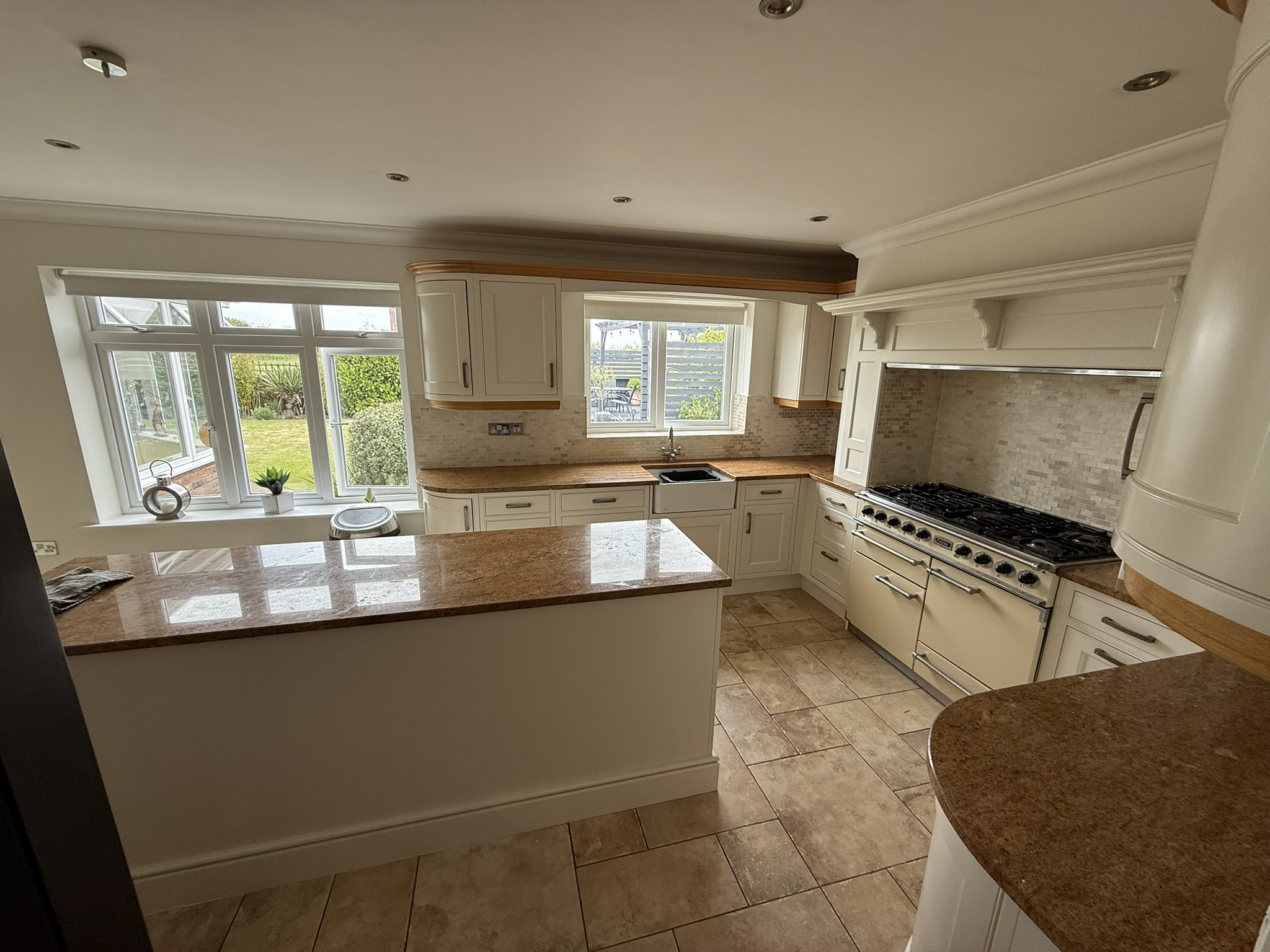 Modern kitchen with cream cabinets, granite worktops, tiled floor, and large windows overlooking the garden